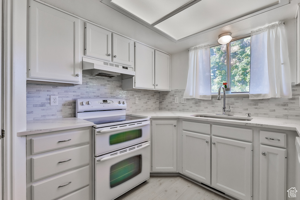 Kitchen with range with two ovens, light hardwood / wood-style flooring, white cabinetry, and sink