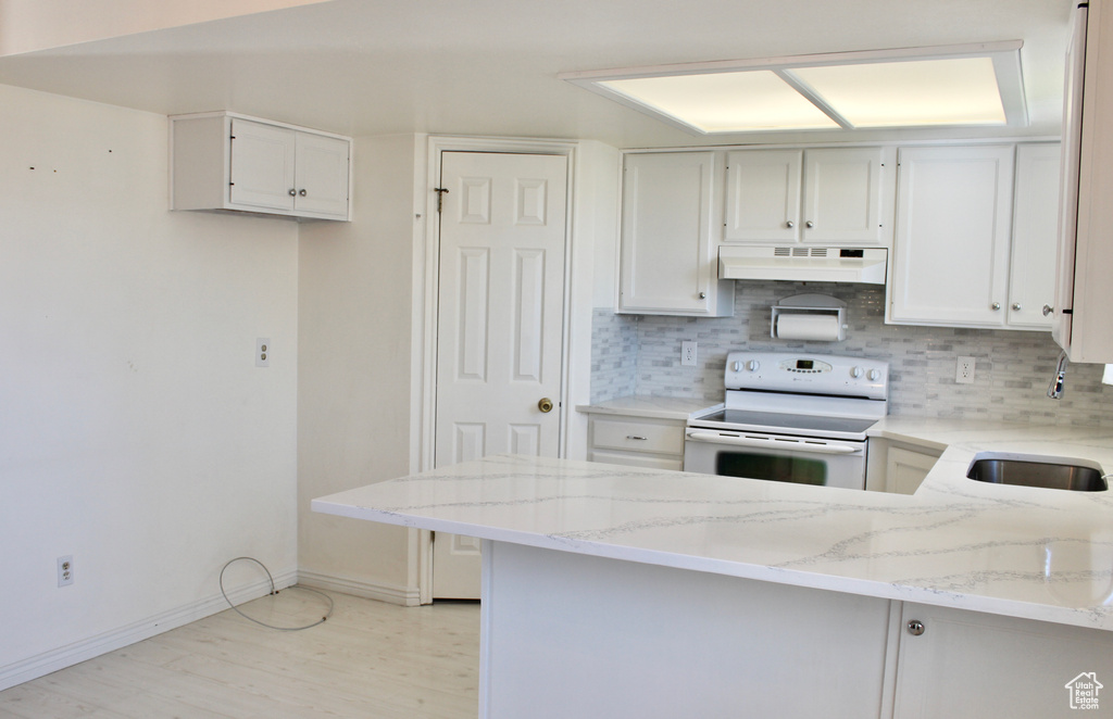 Kitchen featuring white cabinets, light stone counters, premium range hood, and white electric range