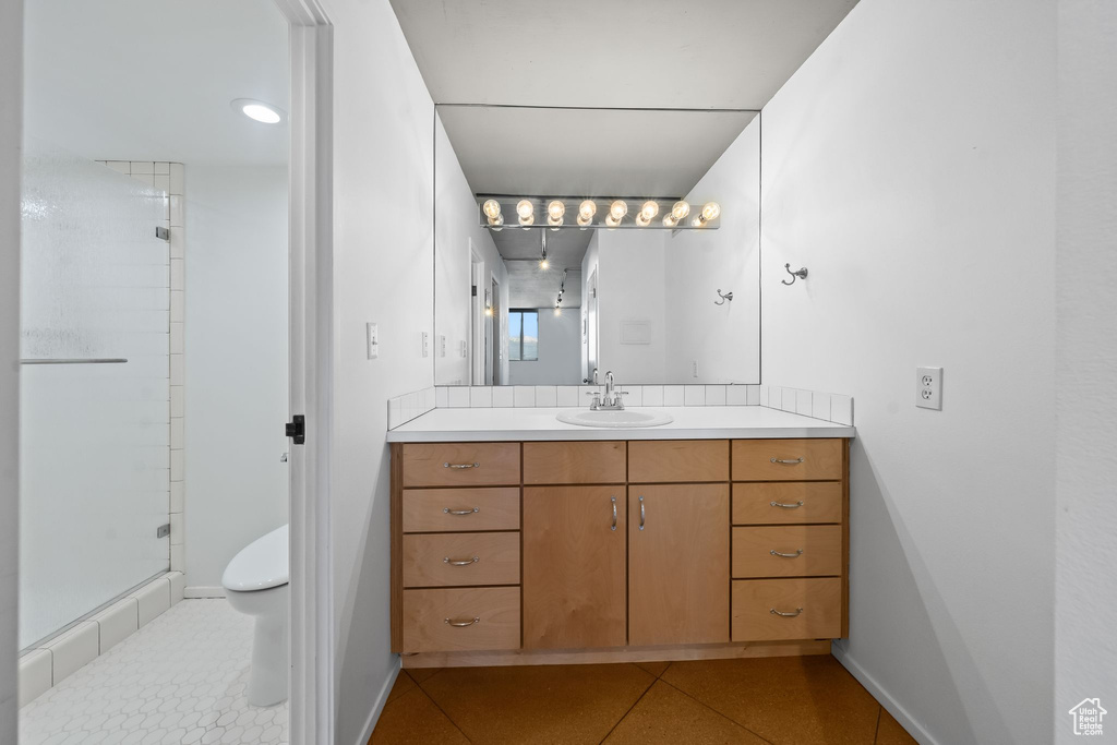 Bathroom featuring large vanity, a shower with shower door, toilet, and tile flooring