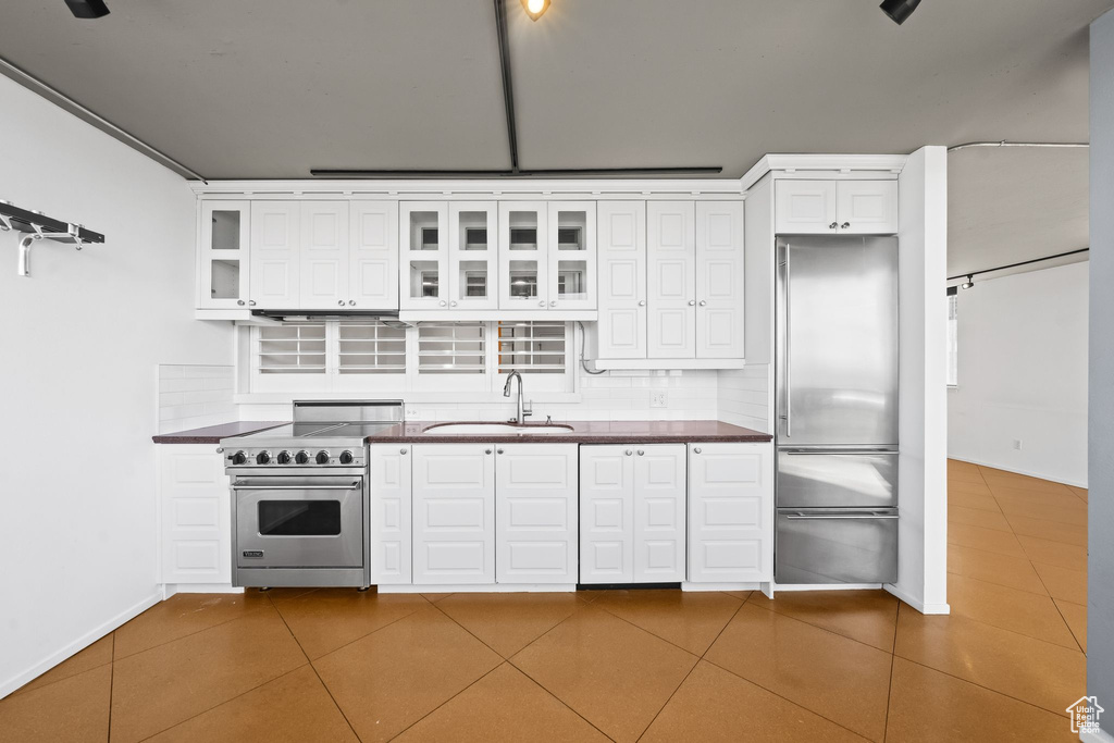 Kitchen featuring light tile floors, premium appliances, white cabinets, sink, and tasteful backsplash