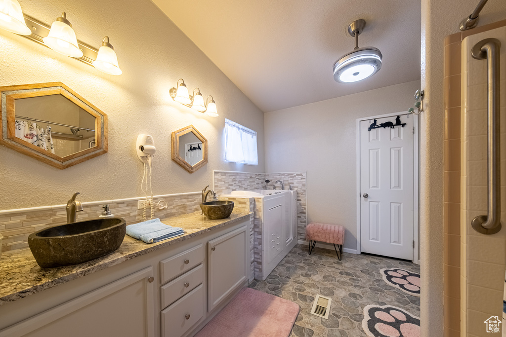 Bathroom featuring tile flooring, large vanity, dual sinks, tasteful backsplash, and lofted ceiling