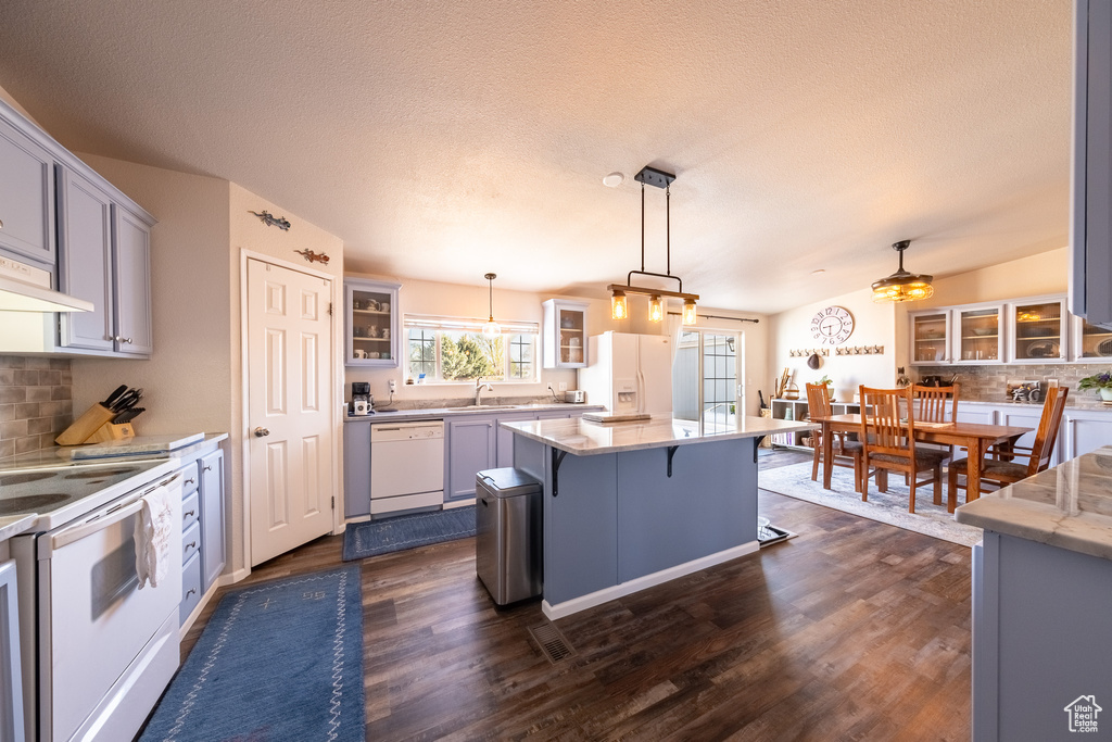 Kitchen featuring white appliances, pendant lighting, a breakfast bar area, and dark wood-type flooring