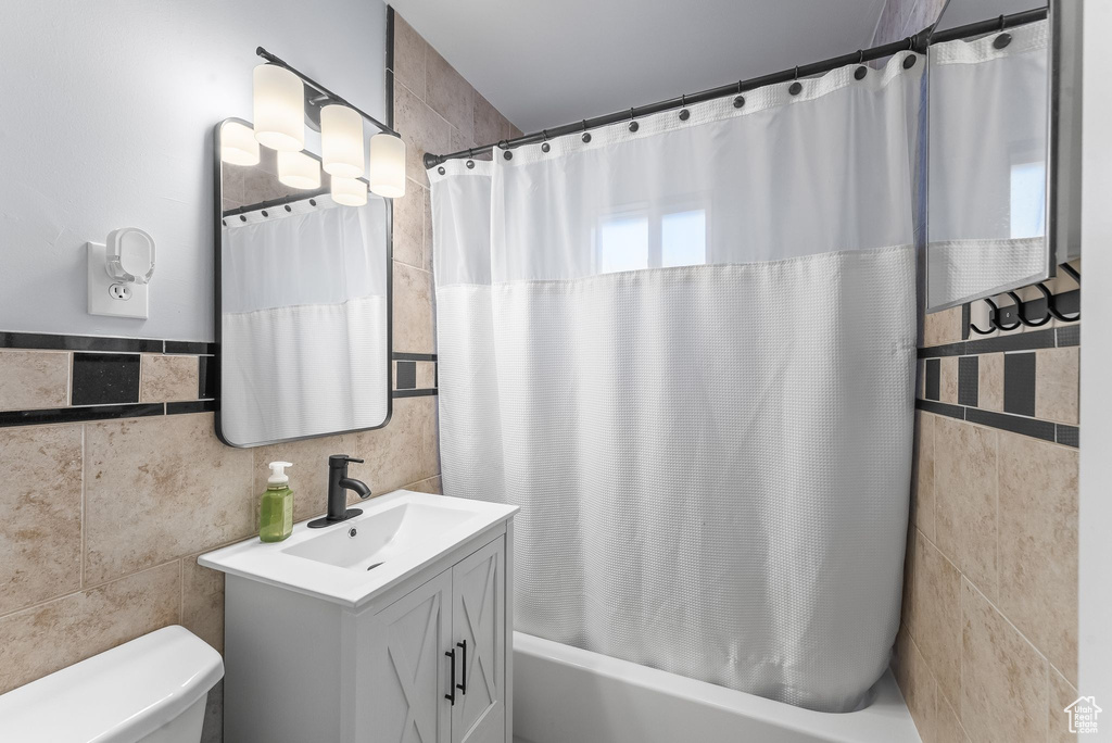 Full bathroom with tile walls, large vanity, shower / bath combination with curtain, and toilet