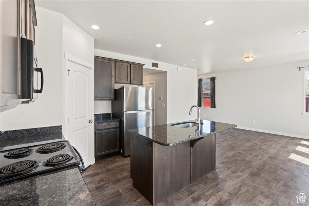 Kitchen featuring sink, dark stone counters, stainless steel fridge, dark hardwood / wood-style floors, and a center island with sink