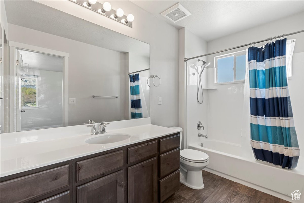 Full bathroom with wood-type flooring, shower / bath combination with curtain, large vanity, and a wealth of natural light