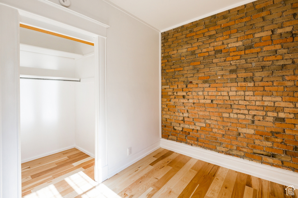 Spare room with brick wall, crown molding, and light wood-type flooring