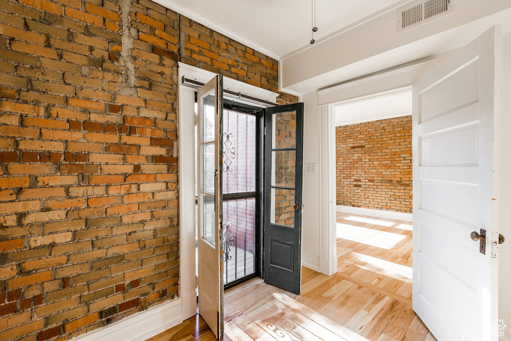 Foyer with brick wall and light hardwood / wood-style floors