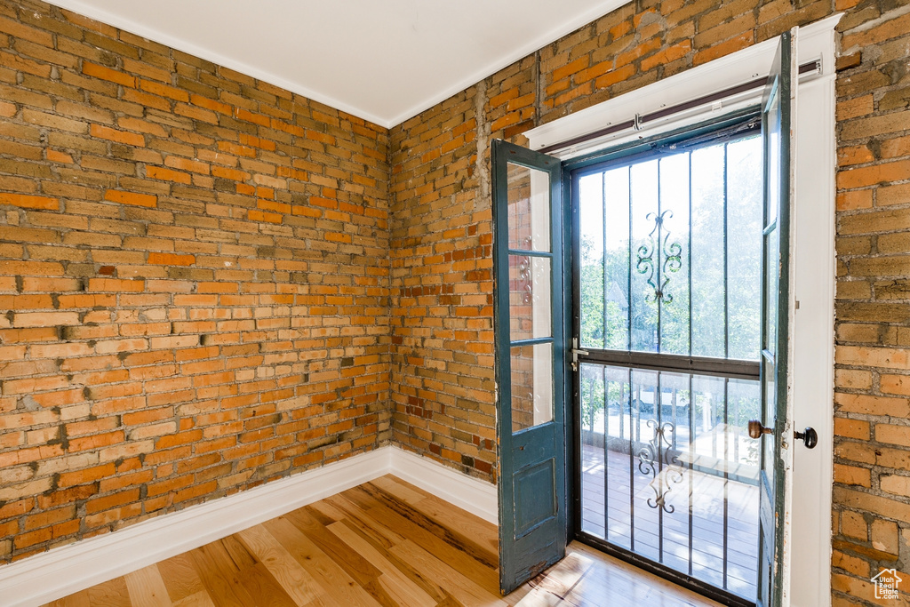 Doorway to outside with plenty of natural light, light hardwood / wood-style floors, and brick wall