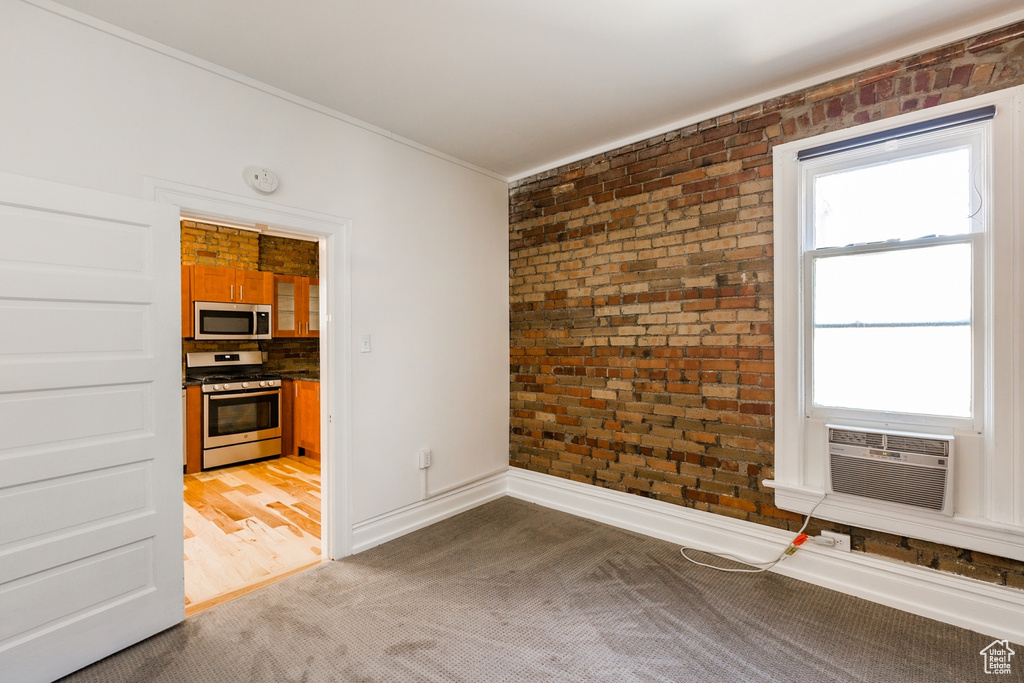 Unfurnished room featuring a wealth of natural light, dark colored carpet, brick wall, and ornamental molding