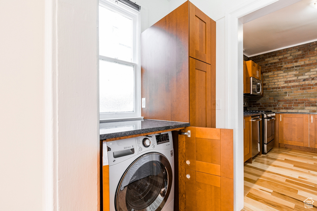 Laundry room with brick wall, light wood-type flooring, and washer / clothes dryer