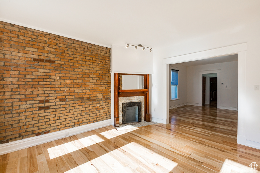 Unfurnished living room with light hardwood / wood-style flooring, brick wall, and track lighting