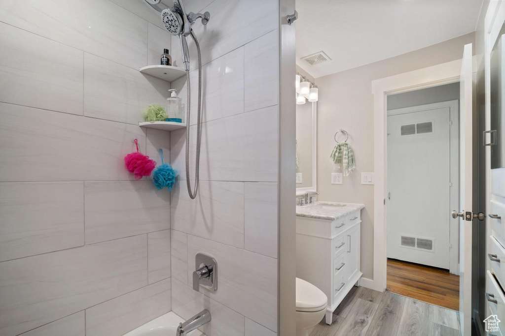 Full bathroom featuring hardwood / wood-style flooring, tiled shower / bath, toilet, and oversized vanity