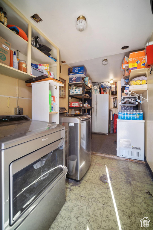 Kitchen featuring tile countertops, white refrigerator with ice dispenser, light tile floors, and washing machine and clothes dryer