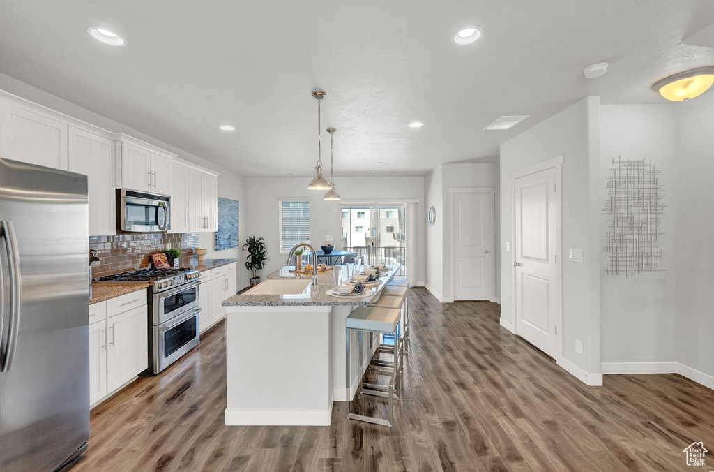 Kitchen featuring pendant lighting, white cabinets, hardwood / wood-style floors, appliances with stainless steel finishes, and an island with sink