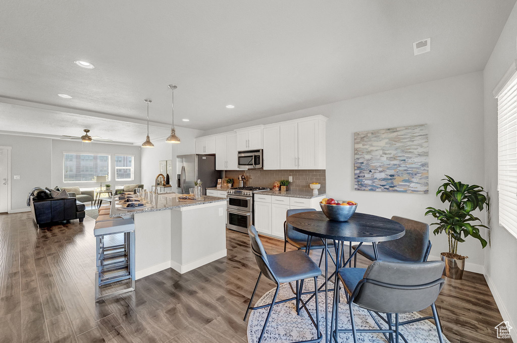 Interior space featuring appliances with stainless steel finishes, pendant lighting, a breakfast bar, dark hardwood / wood-style floors, and a kitchen island with sink