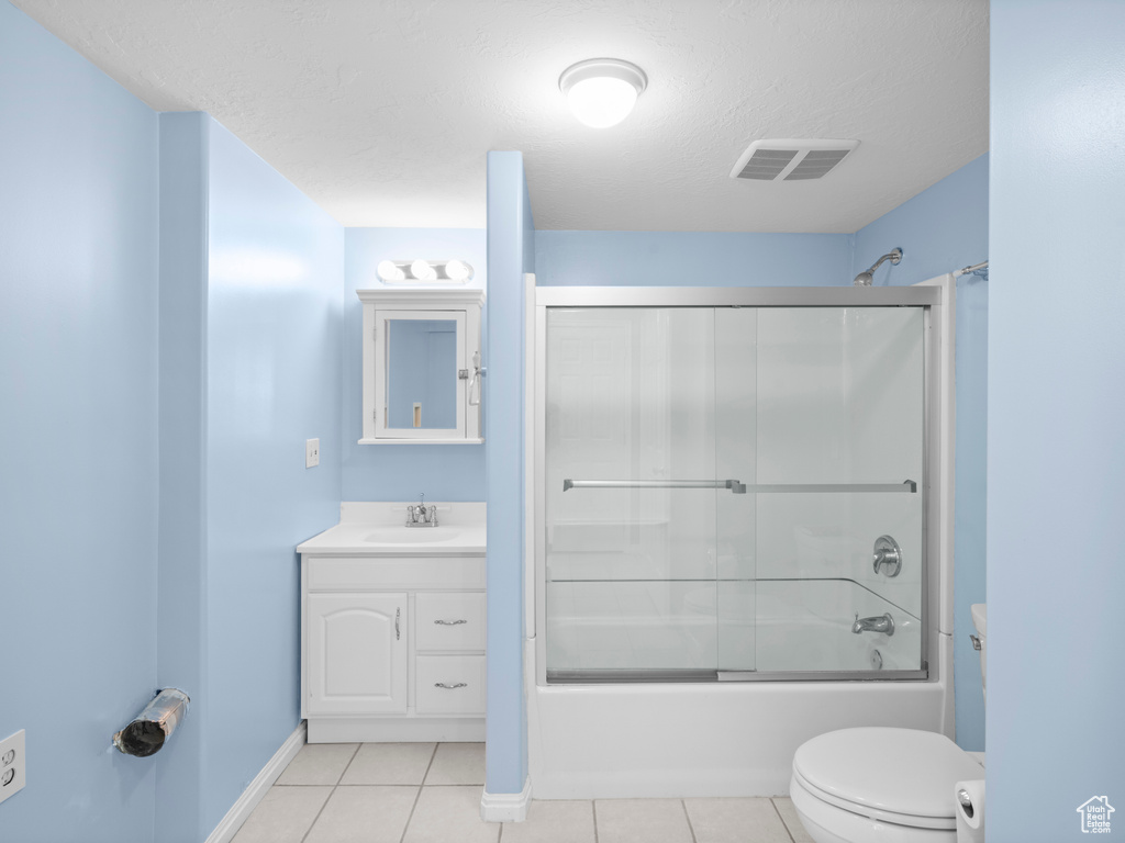 Full bathroom with enclosed tub / shower combo, tile floors, vanity, and toilet