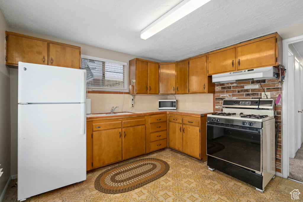 Kitchen with sink, tasteful backsplash, white appliances, and light tile floors