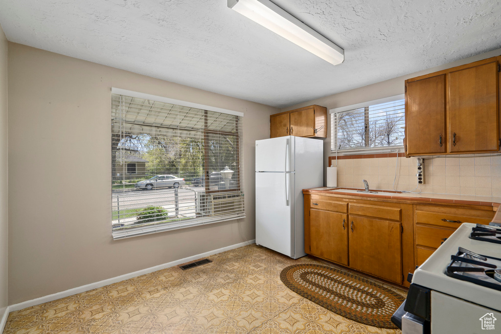 Kitchen featuring light tile floors, a textured ceiling, sink, white appliances, and tasteful backsplash