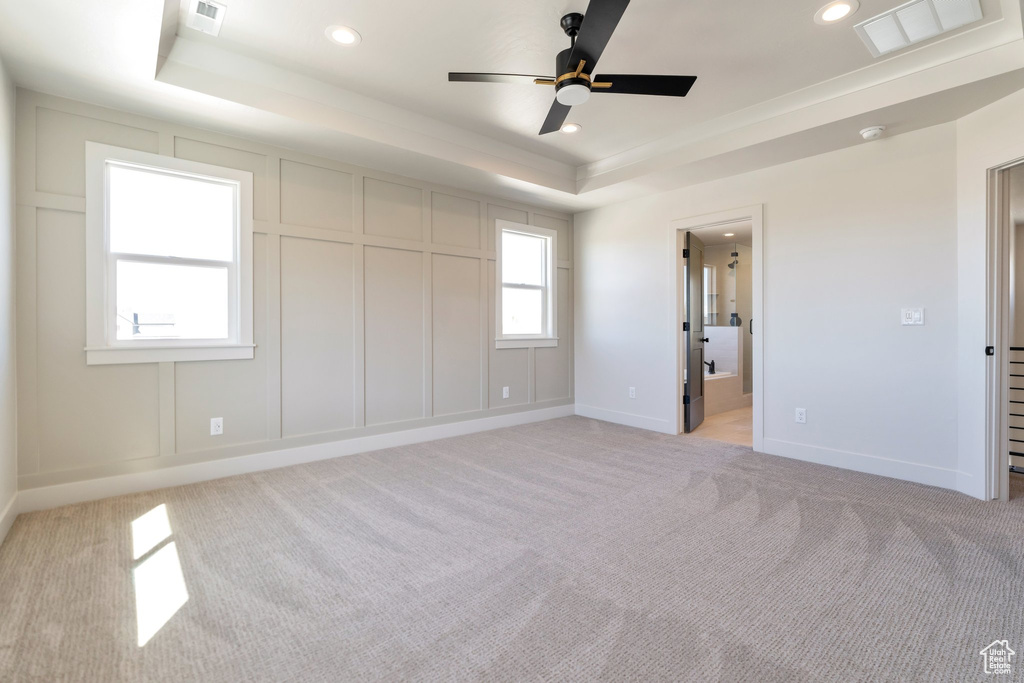 Unfurnished bedroom featuring light colored carpet, a raised ceiling, ceiling fan, and ensuite bath