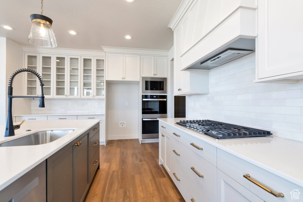 Kitchen with stainless steel appliances, backsplash, white cabinetry, and pendant lighting