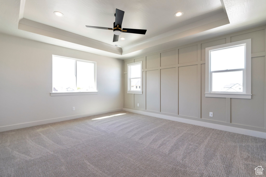 Carpeted spare room featuring ceiling fan and a tray ceiling