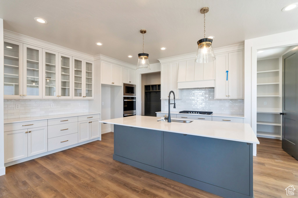 Kitchen with hanging light fixtures, dark hardwood / wood-style flooring, white cabinetry, appliances with stainless steel finishes, and tasteful backsplash