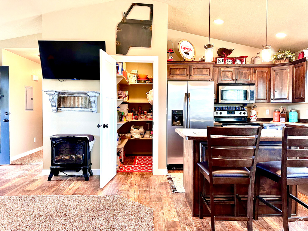 Kitchen with a breakfast bar, light hardwood / wood-style floors, stainless steel appliances, vaulted ceiling, and a wood stove