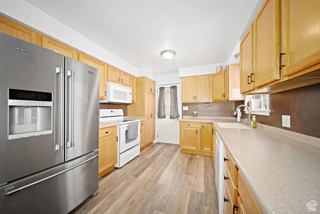 Kitchen with light brown cabinetry, sink, white appliances, and light wood-type flooring