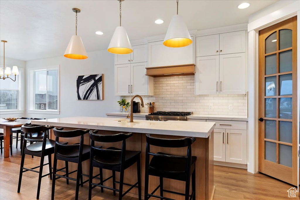 Kitchen featuring hanging light fixtures, a breakfast bar area, light hardwood / wood-style floors, a kitchen island with sink, and white cabinetry