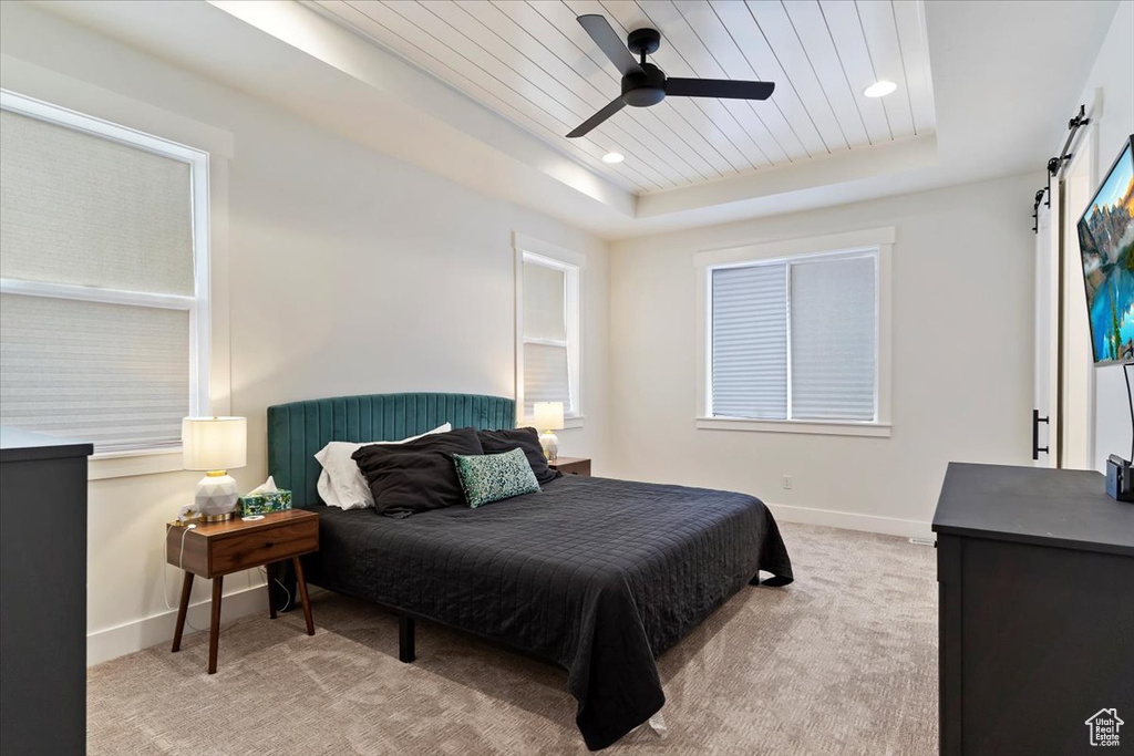 Bedroom featuring light colored carpet, a raised ceiling, ceiling fan, and a barn door