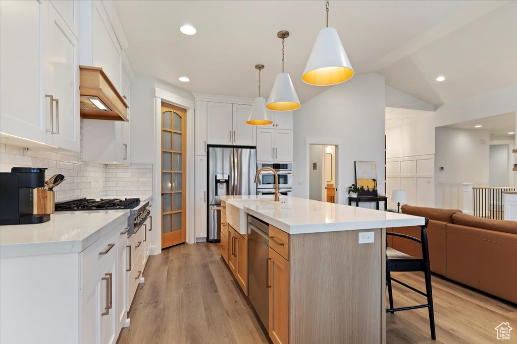 Kitchen featuring white cabinets, backsplash, decorative light fixtures, light hardwood / wood-style flooring, and a kitchen island with sink