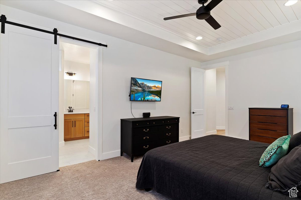 Bedroom featuring light carpet, connected bathroom, a tray ceiling, a barn door, and ceiling fan
