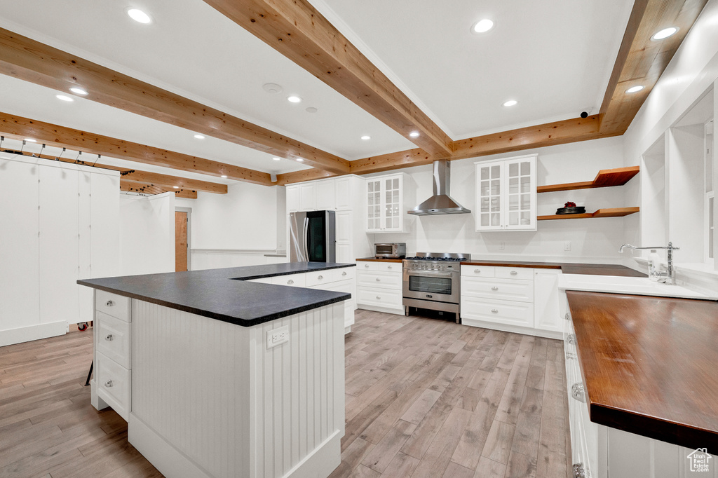 Kitchen featuring white cabinets, wall chimney range hood, light wood-type flooring, and stainless steel appliances