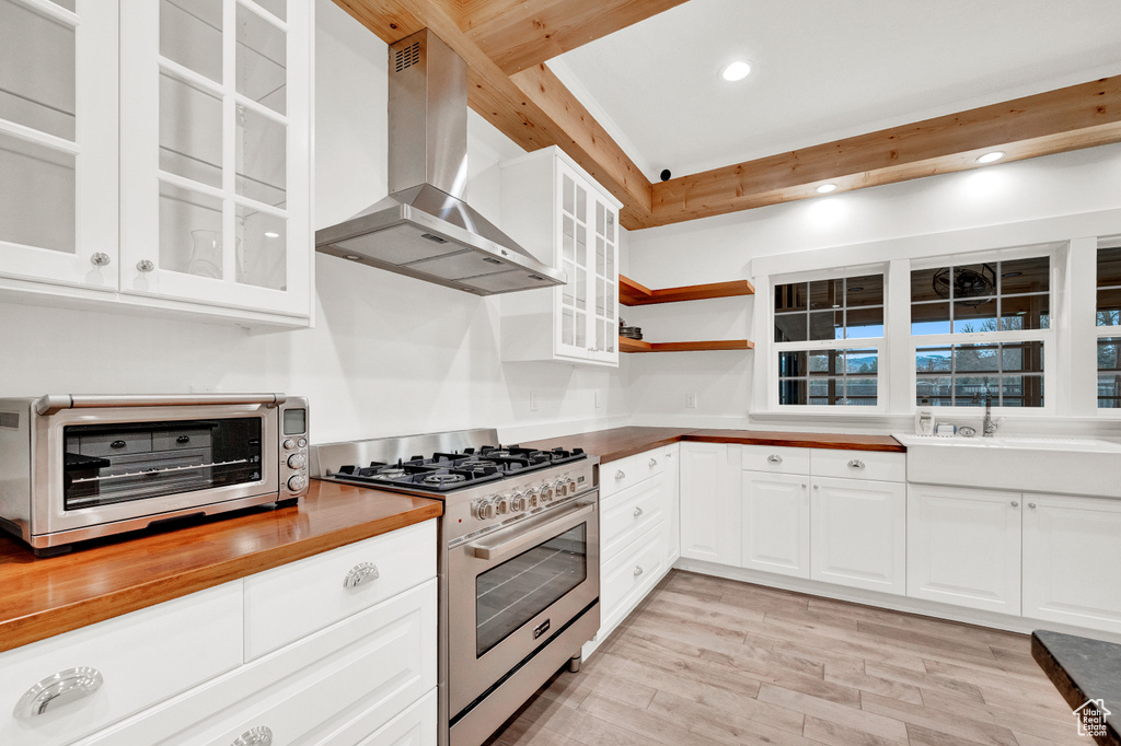 Kitchen featuring white cabinets, light hardwood / wood-style flooring, wall chimney range hood, beam ceiling, and high end range