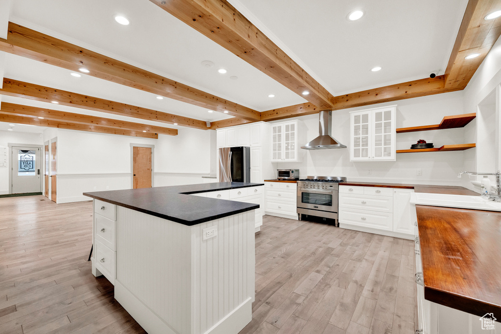 Kitchen featuring wall chimney exhaust hood, light wood-type flooring, white cabinetry, stainless steel appliances, and sink