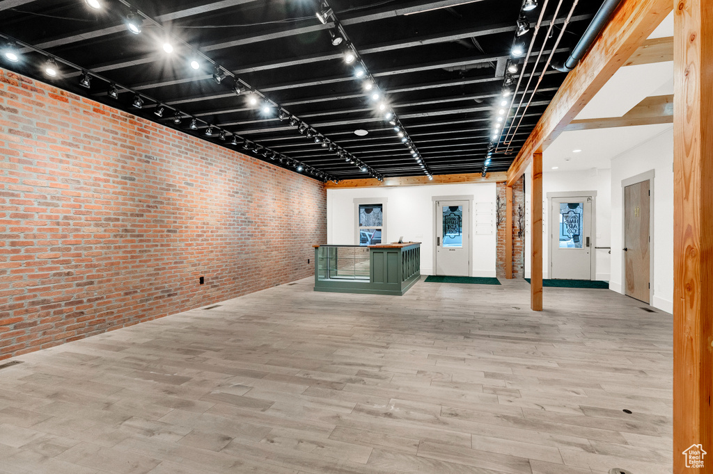 Basement with brick wall, light hardwood / wood-style flooring, and track lighting