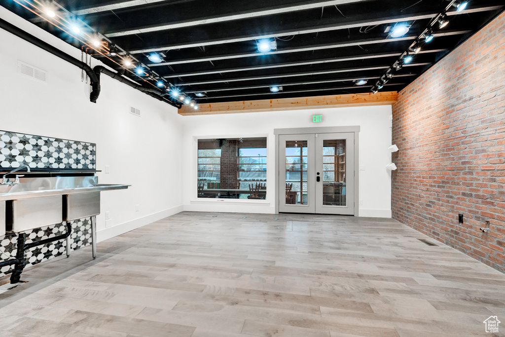 Basement featuring brick wall, french doors, light hardwood / wood-style flooring, and track lighting