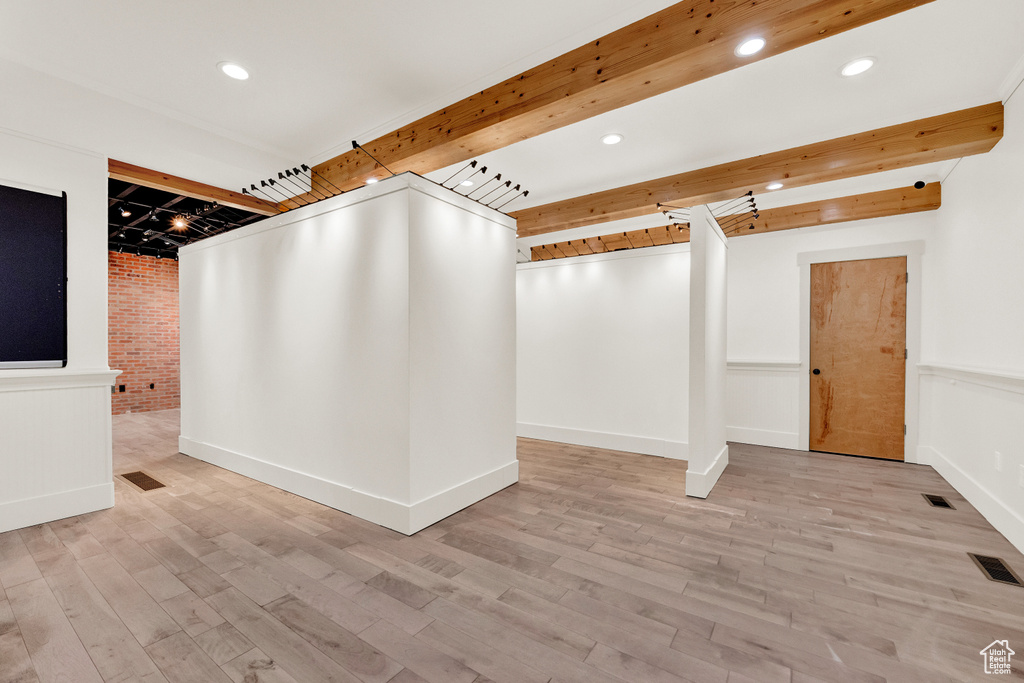 Interior space with beamed ceiling, light hardwood / wood-style floors, and brick wall
