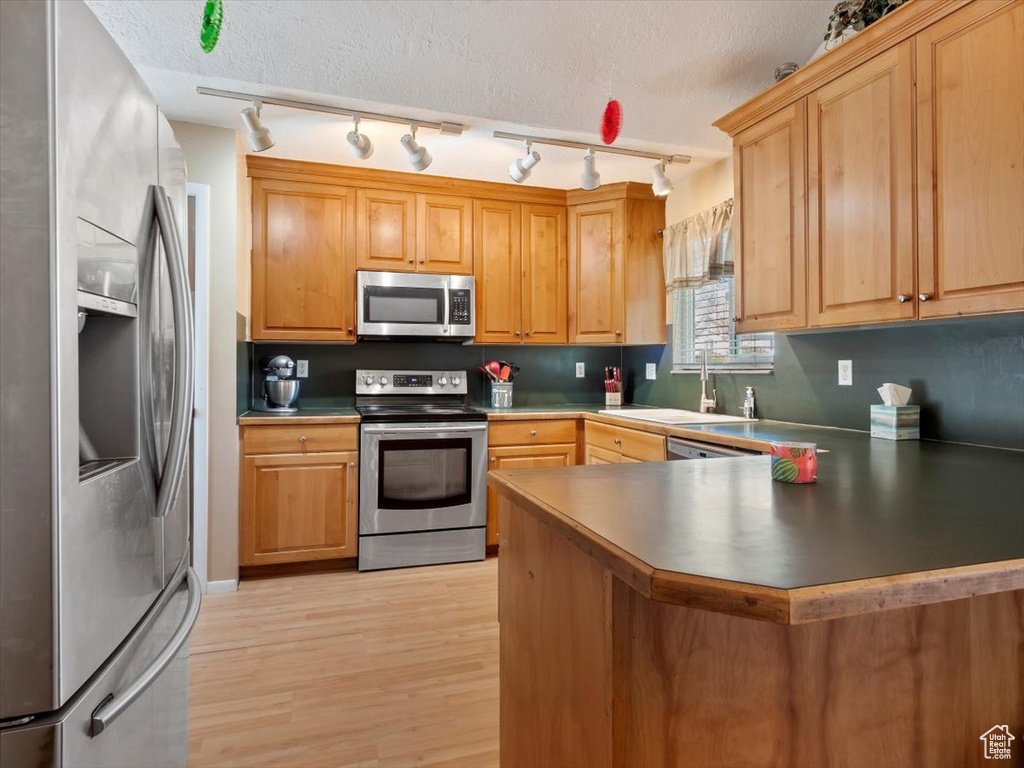 Kitchen featuring light wood-type flooring, rail lighting, kitchen peninsula, stainless steel appliances, and sink