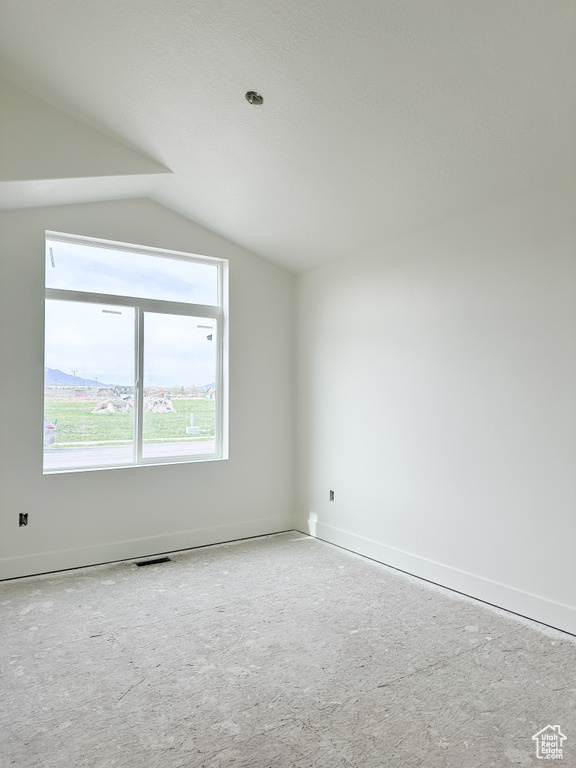 Spare room featuring light colored carpet and lofted ceiling