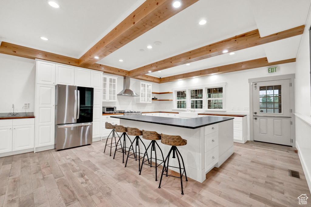 Kitchen with white cabinets, a kitchen island, wall chimney exhaust hood, and stainless steel fridge