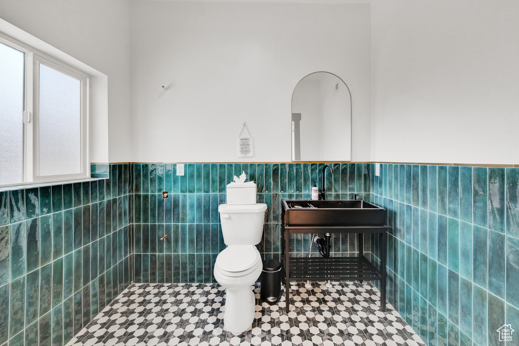 Bathroom featuring toilet, tile floors, tile walls, and sink