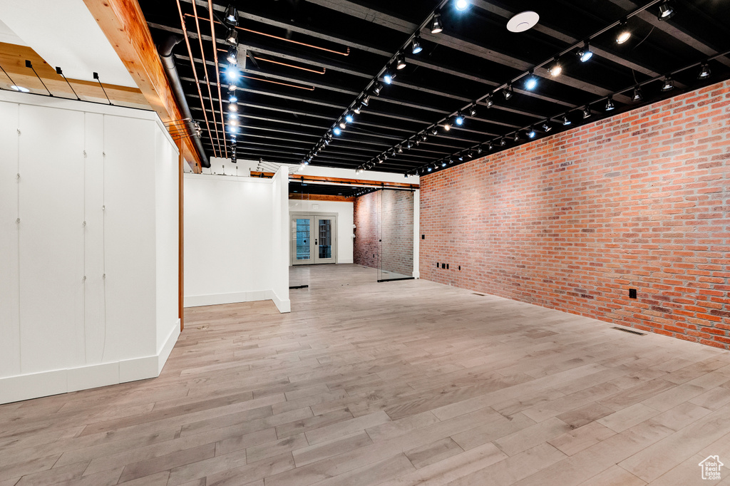 Basement with light hardwood / wood-style floors, brick wall, and rail lighting