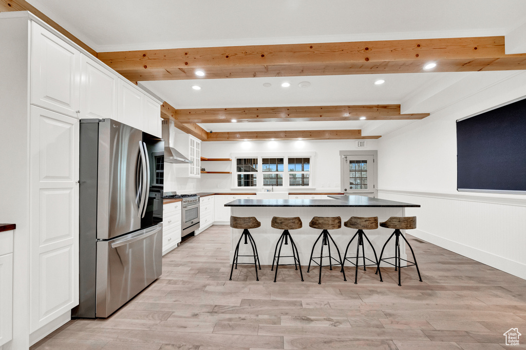 Kitchen with white cabinets, appliances with stainless steel finishes, beam ceiling, and a breakfast bar