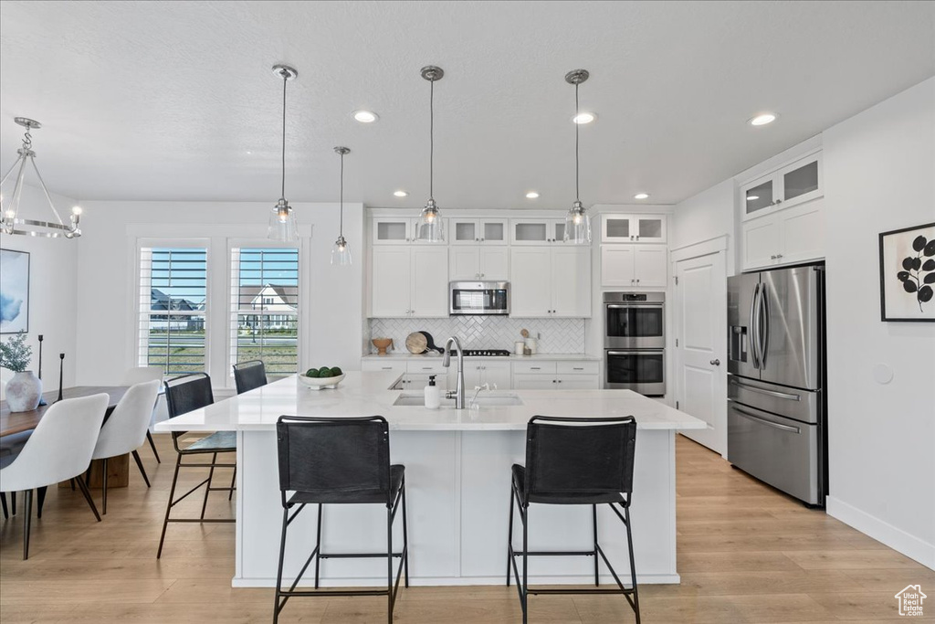Kitchen with appliances with stainless steel finishes, light hardwood / wood-style flooring, a breakfast bar area, a center island with sink, and pendant lighting