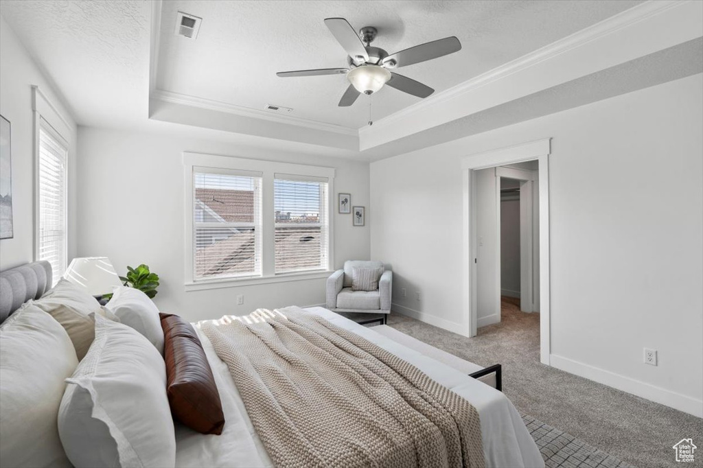 Bedroom featuring a raised ceiling, ceiling fan, light carpet, and ornamental molding