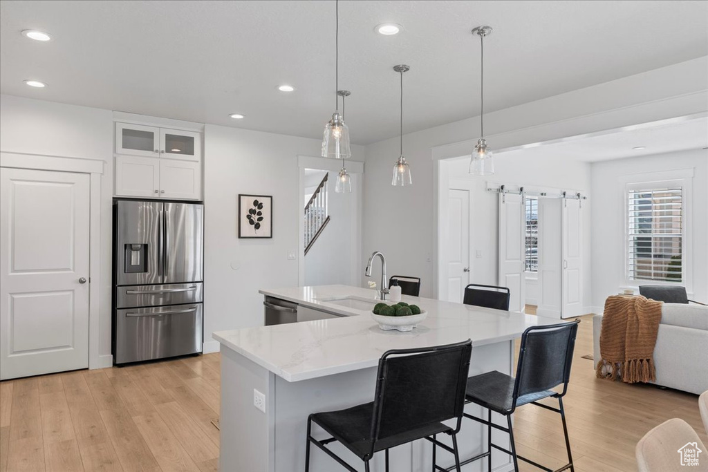 Kitchen featuring decorative light fixtures, white cabinets, light hardwood / wood-style flooring, appliances with stainless steel finishes, and sink
