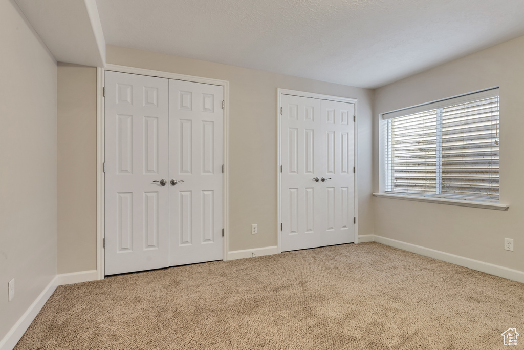Unfurnished bedroom with light colored carpet and multiple closets