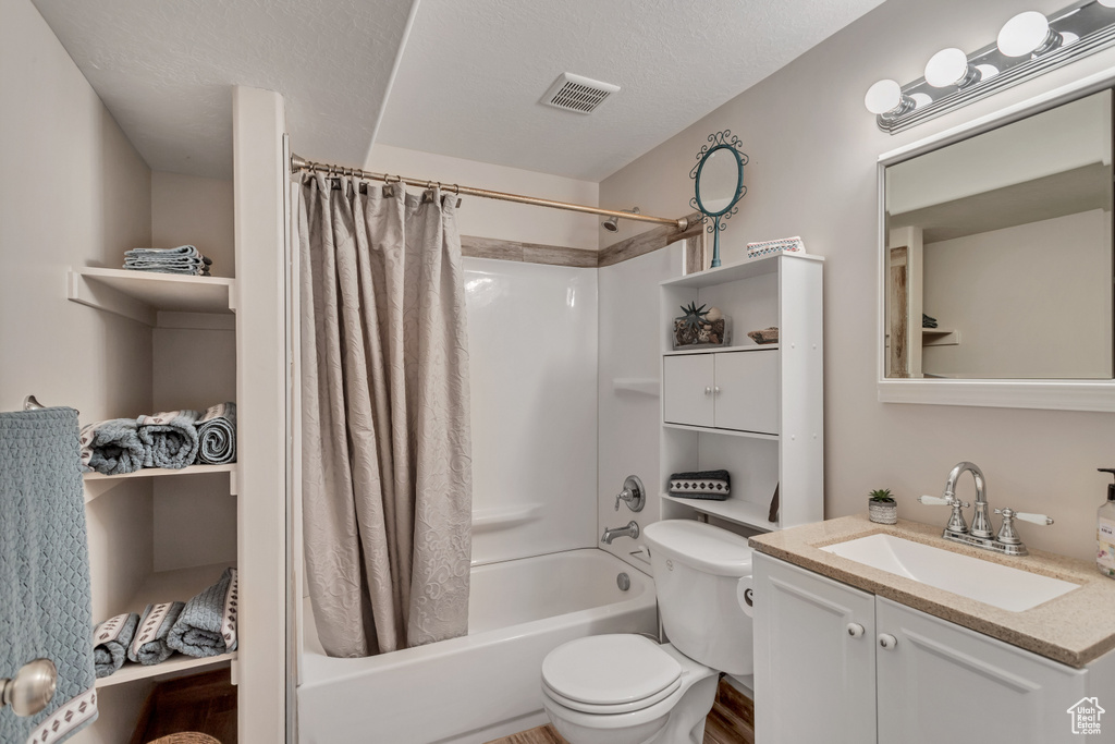 Full bathroom featuring vanity, shower / bath combo, toilet, and a textured ceiling
