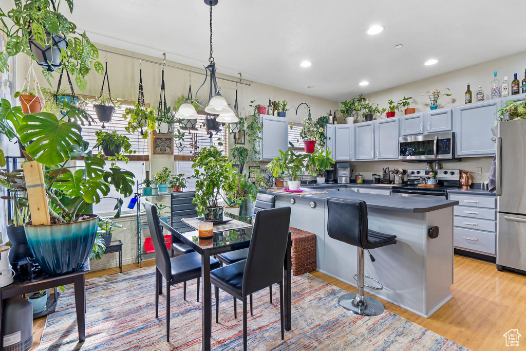 Kitchen featuring light hardwood / wood-style floors, pendant lighting, stainless steel appliances, and a breakfast bar area